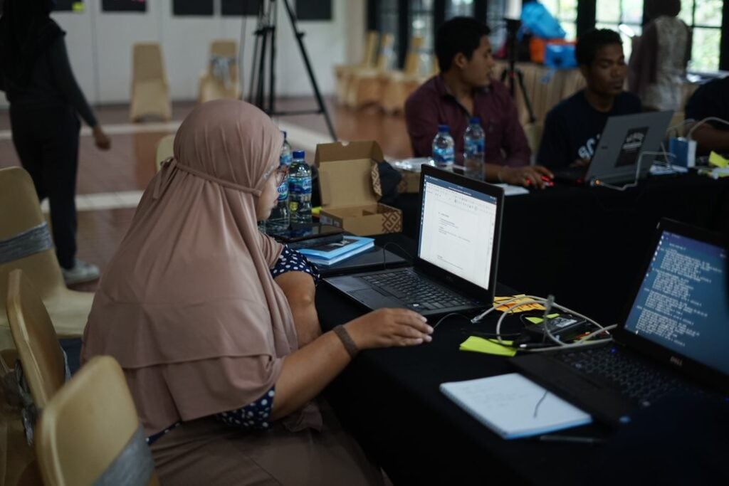 An image of a woman in a head scarf working at a laptop computer, at the School of Community Networking in Indonesia.